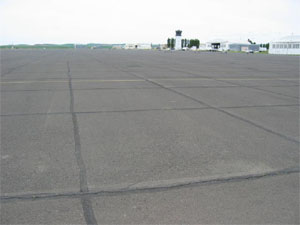 Overview photo of an apron pavement with a uniform rectangular pattern of low-severity           transverse and longitudinal cracks.  The pattern is the result of cracks that have reflected through the asphalt surface at the joints of the PCC slabs below.