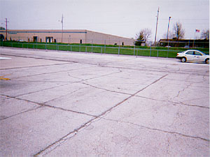 Overview photo of an apron pavement with a uniform rectangular pattern of medium-severity           transverse and longitudinal cracks.  The pattern is the result of cracks that have reflected through the asphalt surface at the joints of the PCC slabs below.  Some spalling is visible at the cracks.