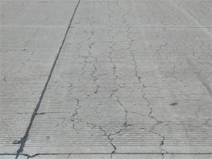 Overview photo of a PCC slab with a noticeable pattern of fine cracks spread over the entire surface area of the slab.            Some of the cracks are spalled.