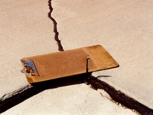 Close-up photo showing a transverse joint with a 1 1/2 in (38 mm) difference in elevation across the joint.            A clipboard is placed across the joint in the photo to illustrate that there is a height differential between the two slabs.