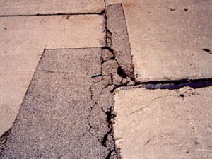 Close-up photo of an irregularly shaped asphalt patch within a PCC slab.  The patch           contains considerable visible distress that includes spalling, cracking, and a noticeable loss of material.